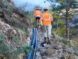 Équipe de chantier progressant le long de canalisations posées sur un terrain escarpé.